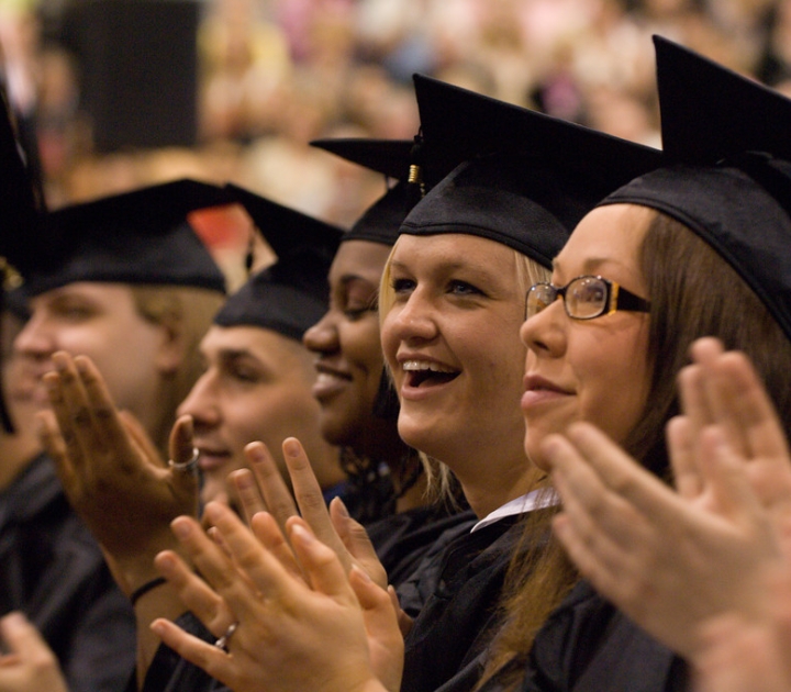 Students in caps and gowns applauding at commencement 